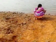 Mujer india orinando en la tierra junto a un lago